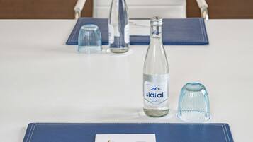 Una mesa con un cuaderno, un bolígrafo, una botella de agua Sidiali y dos vasos.