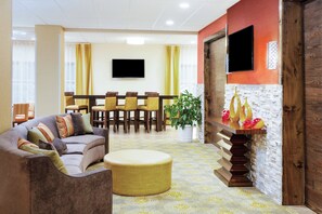 A hotel lobby with a sofa, chairs, a TV, a plant, and a fruit display. - Holiday Inn Express & Suites Sandusky by IHG (Sandusky)