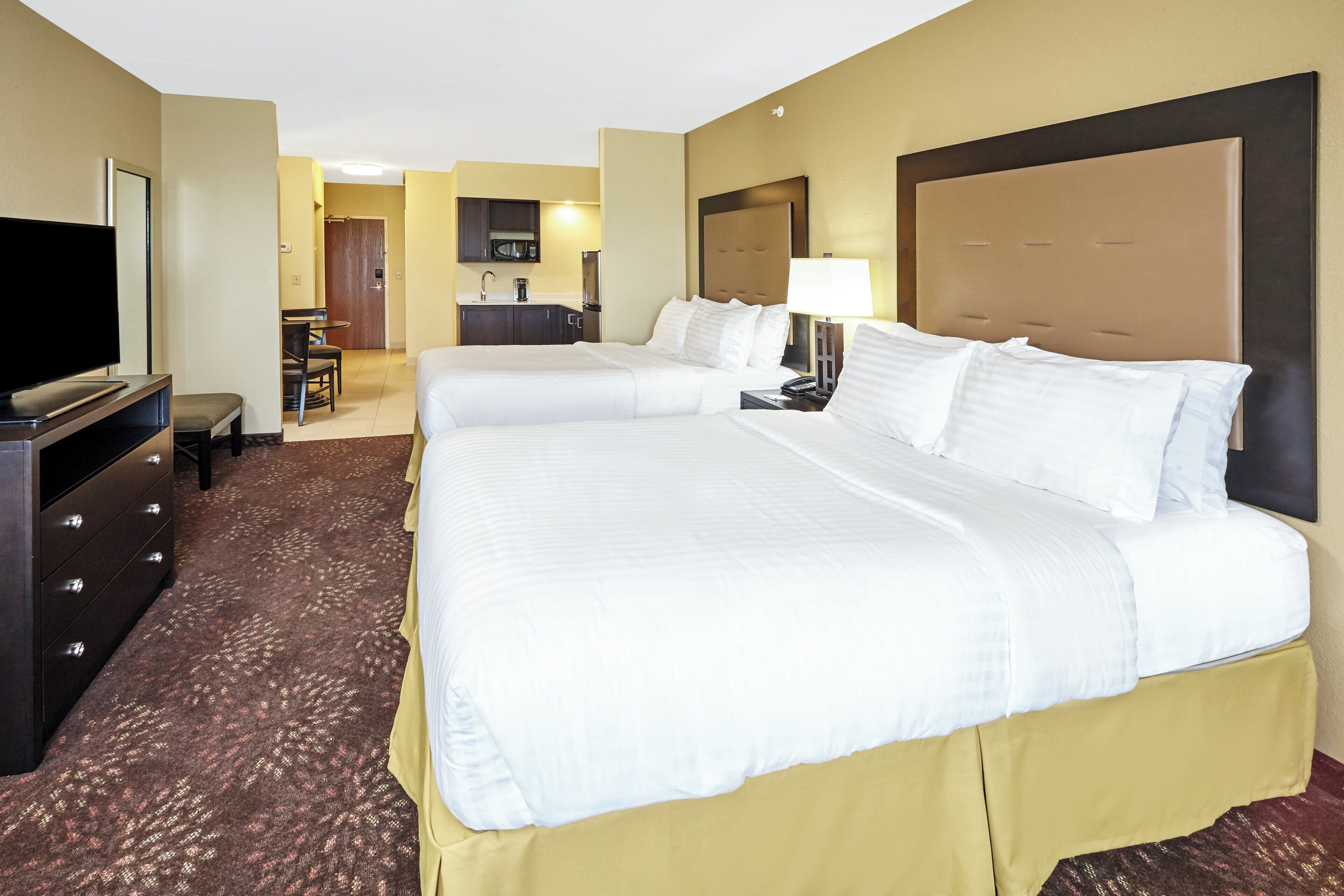 A hotel room with two beds, a TV, a desk, and a bathroom visible in the background.