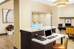 A reception desk with a laptop, a telephone, and a computer monitor. There is a chair and a plant in the room. - Holiday Inn Express & Suites Sandusky by IHG (Sandusky)