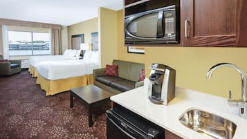 A hotel room with a bed, a sofa, a coffee maker, a microwave, a sink, and a view of a body of water.
