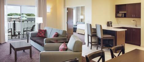 A hotel room with a living area, dining table, and kitchenette. There is a balcony with a view of the city.