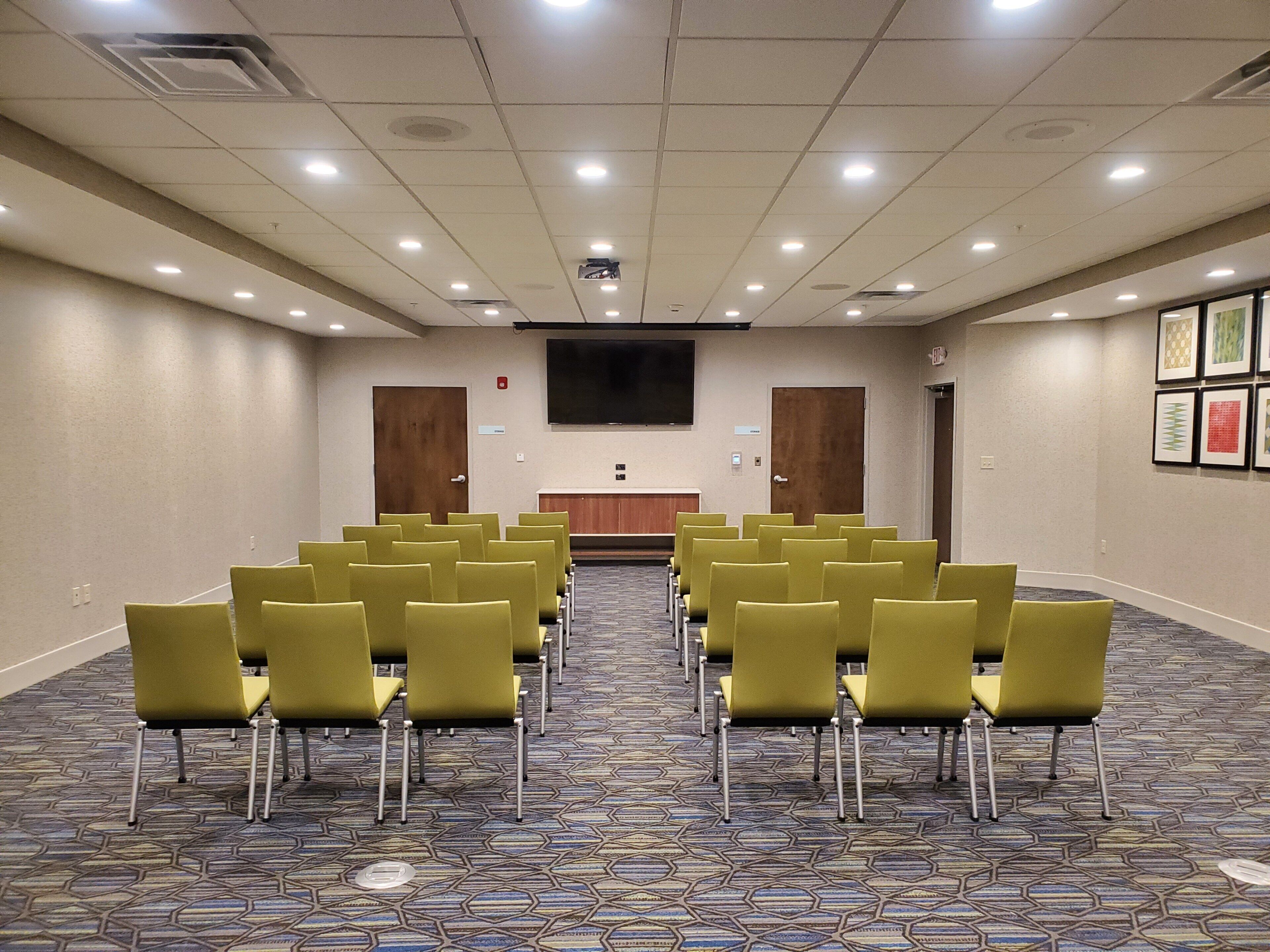 A conference room with rows of chairs, a large screen, and a carpeted floor.