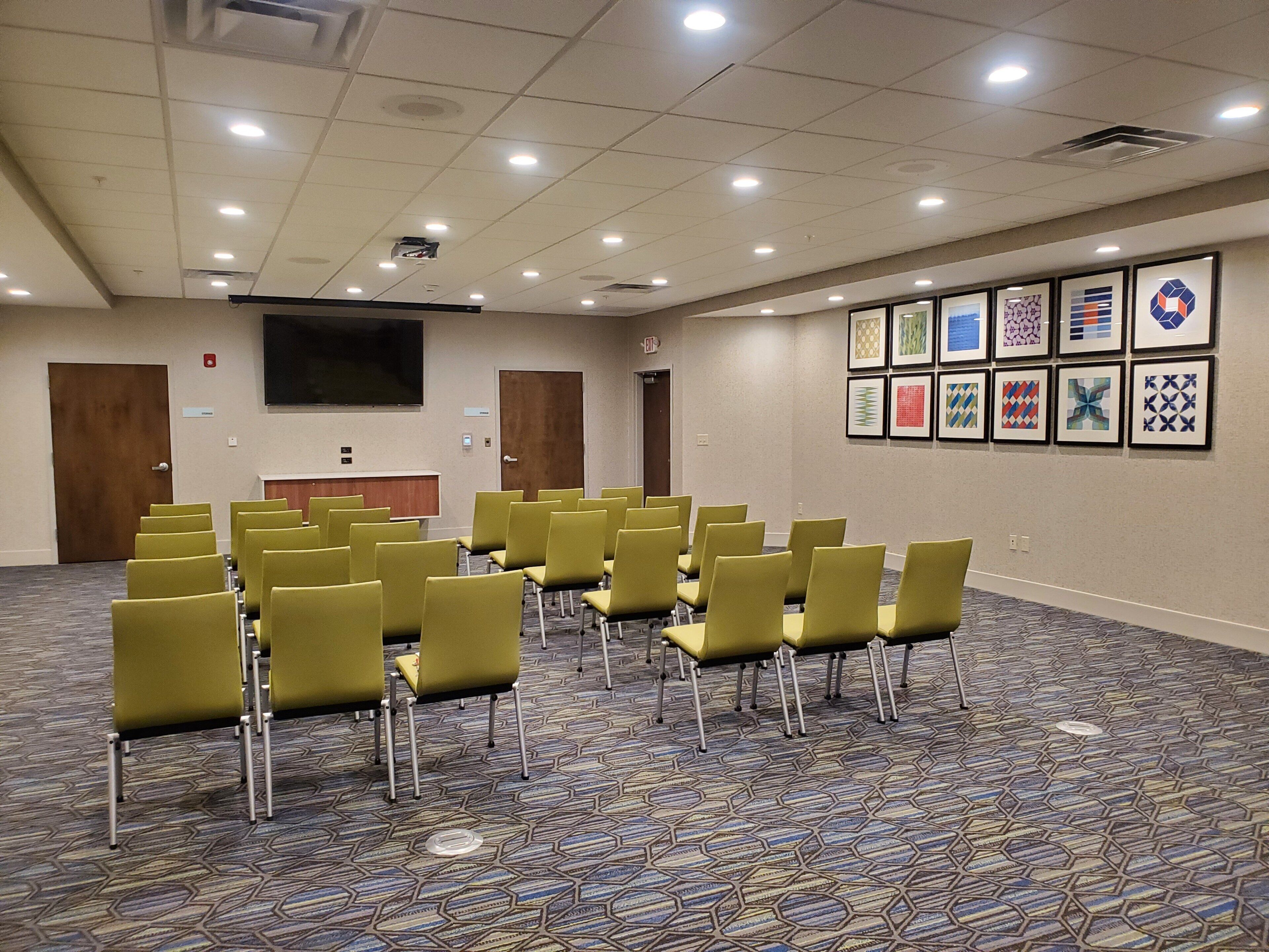 Un salón de conferencias con filas de sillas, un atril, una pantalla y obras de arte enmarcadas en la pared.