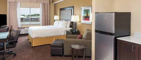 Habitación de hotel con cama, escritorio, silla, refrigerador y vista a un edificio.