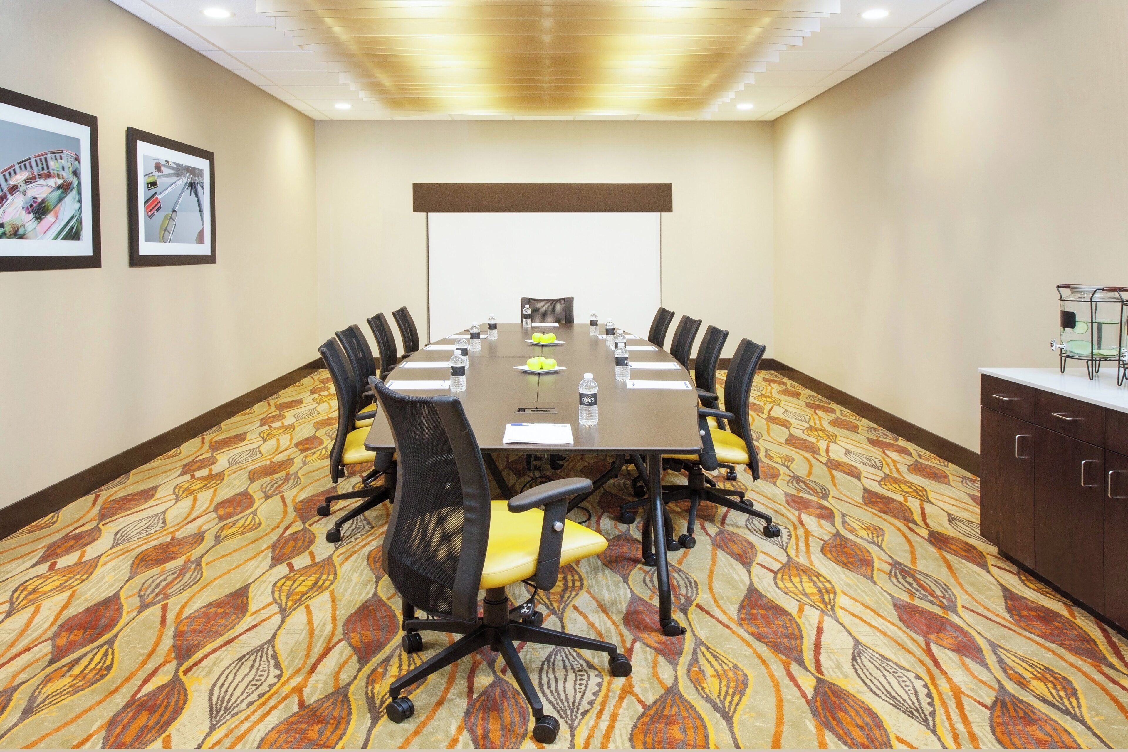 A conference room with a long table, chairs, a projector screen, and a water dispenser.