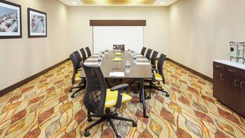 A conference room with a long table, chairs, a projector screen, and a water dispenser.