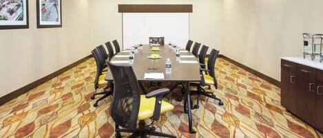 A conference room with a long table, chairs, a projector screen, and a water dispenser.