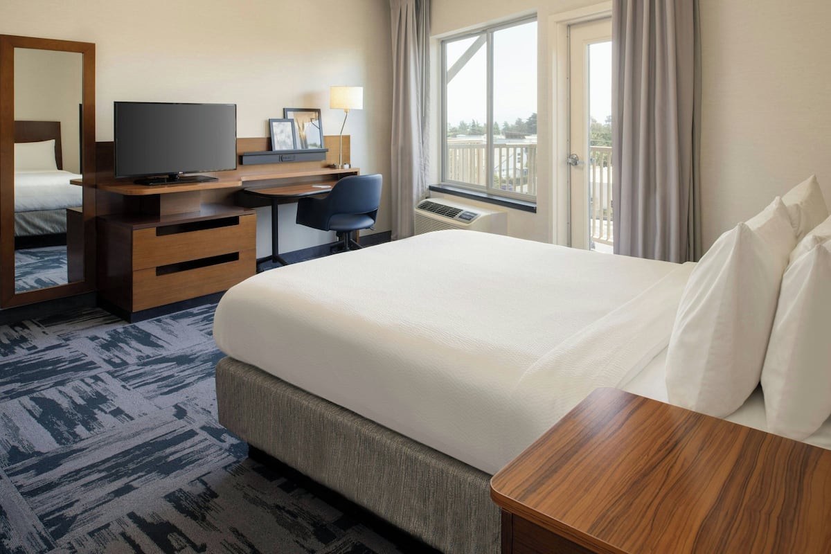 A hotel room with a large bed, a desk with a TV, a chair, a dresser, and a window with curtains.