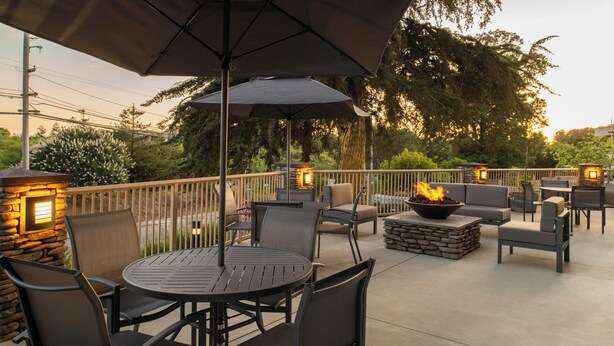 An outdoor patio with round tables and chairs, a stone fireplace, and a railing. - Fairfield Inn & Suites by Marriott Santa Cruz, CA (Santa Cruz)