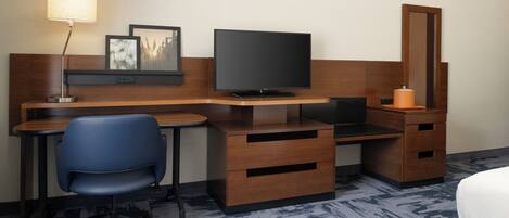 Une chambre d’hôtel avec un bureau en bois, une télévision, une chaise, une commode et un lit.