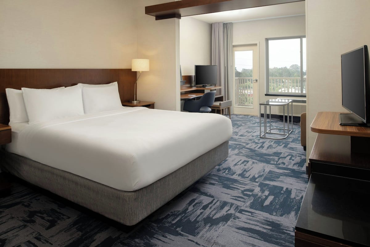 A hotel room with a large bed, a desk with a chair, a television, and a balcony with a view.