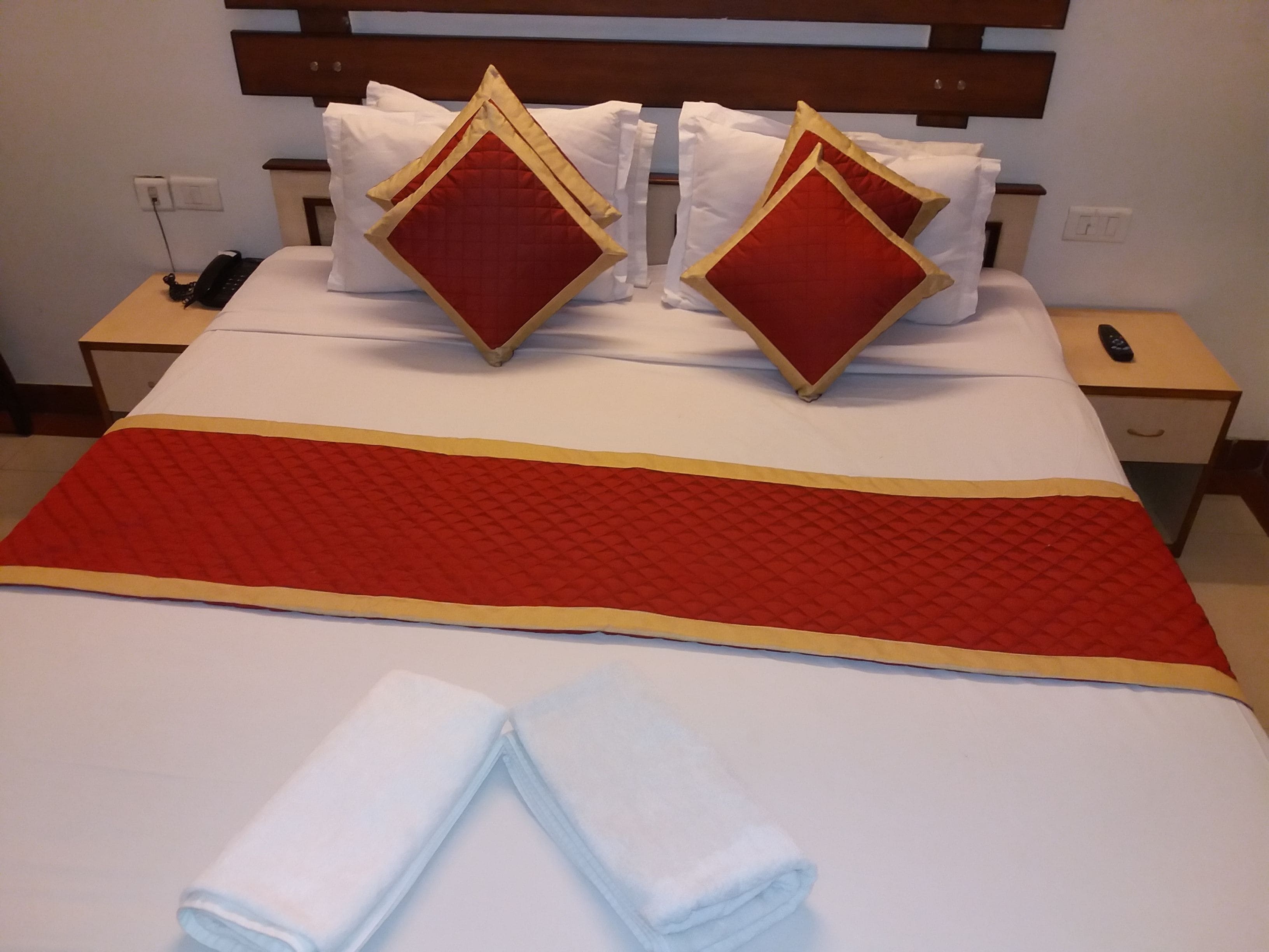 Une chambre d’hôtel avec un lit bien fait, deux oreillers, une table de chevet avec un téléphone et une télécommande sur la table de nuit.