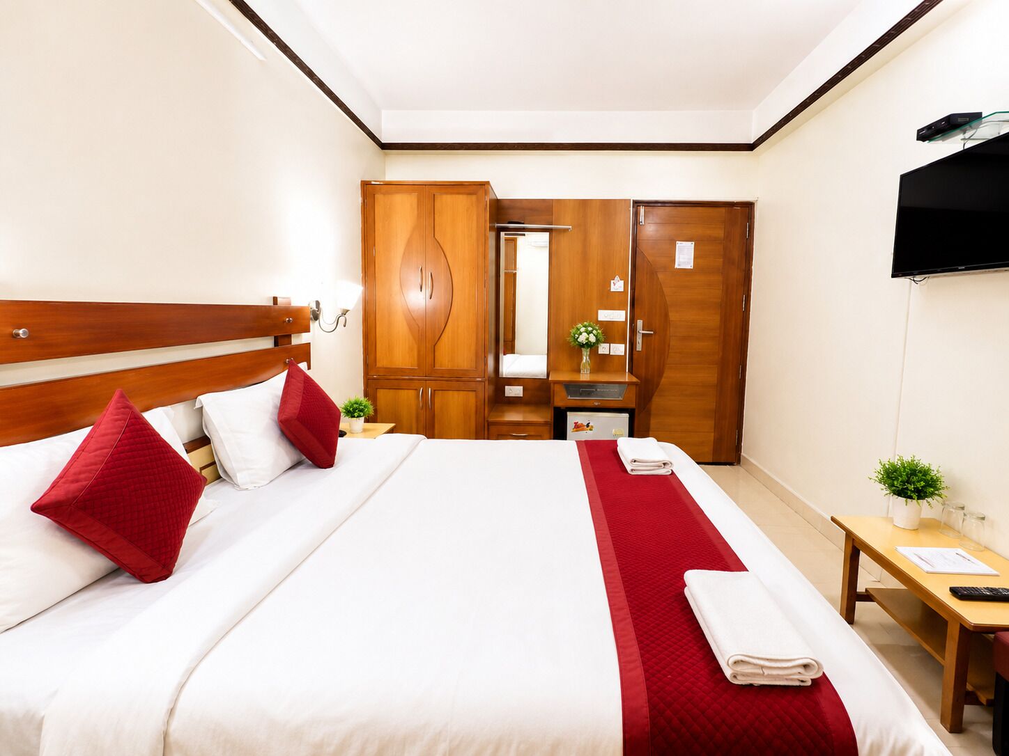 A hotel room with a bed, wardrobe, bedside table, and a TV mounted on the wall.