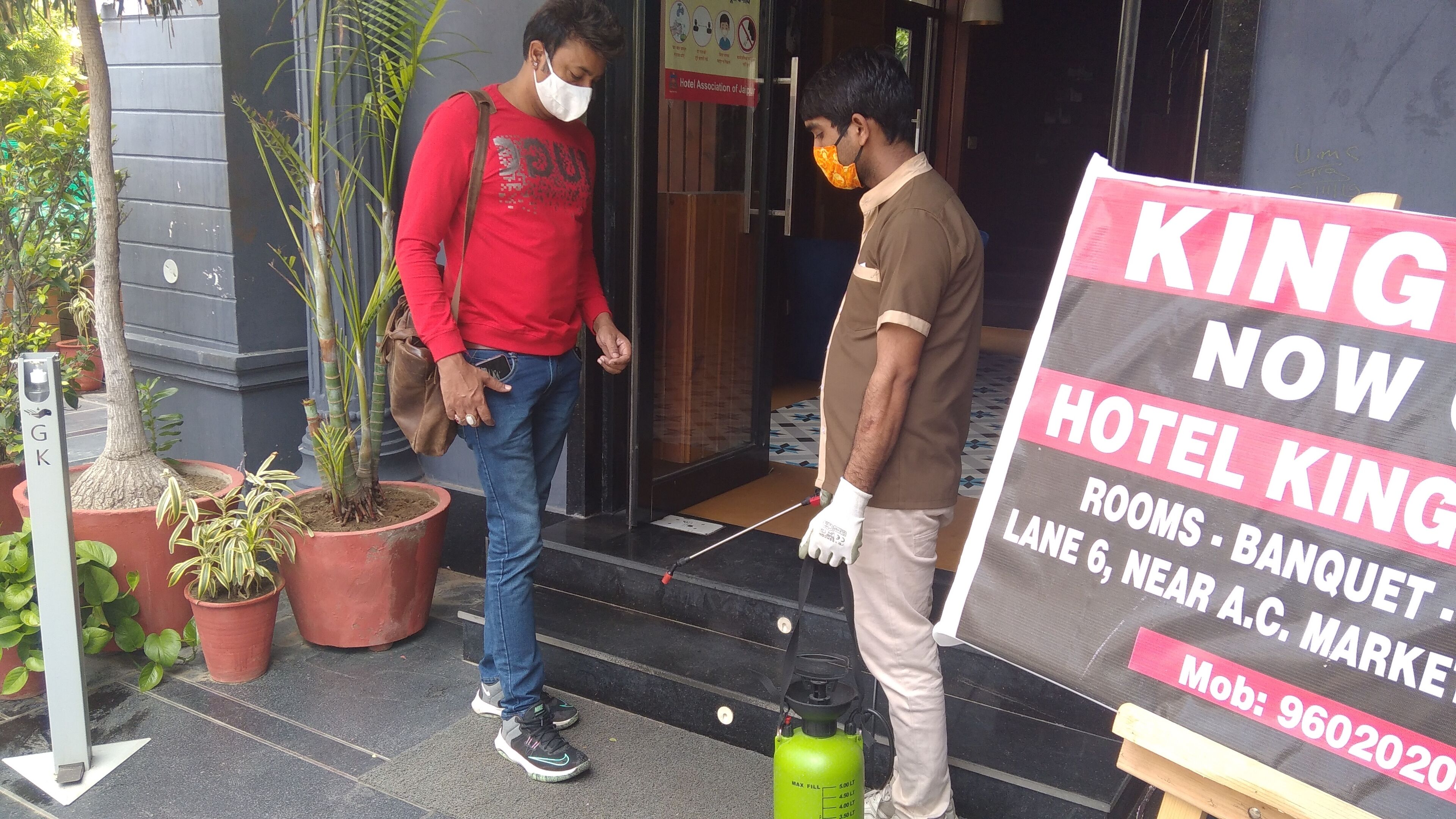Dos hombres de pie frente a la entrada de un hotel, uno sosteniendo un cartel publicitario del hotel.