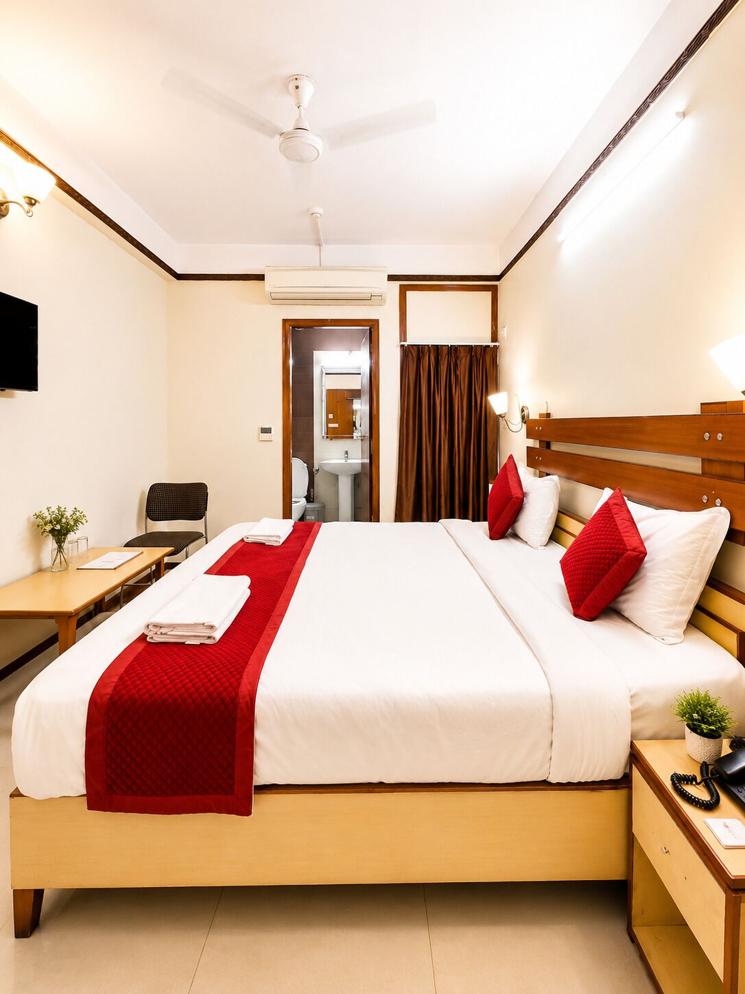 Une chambre d’hôtel avec un lit, un bureau, une chaise, une télévision et une salle de bain visible à travers une porte ouverte.
