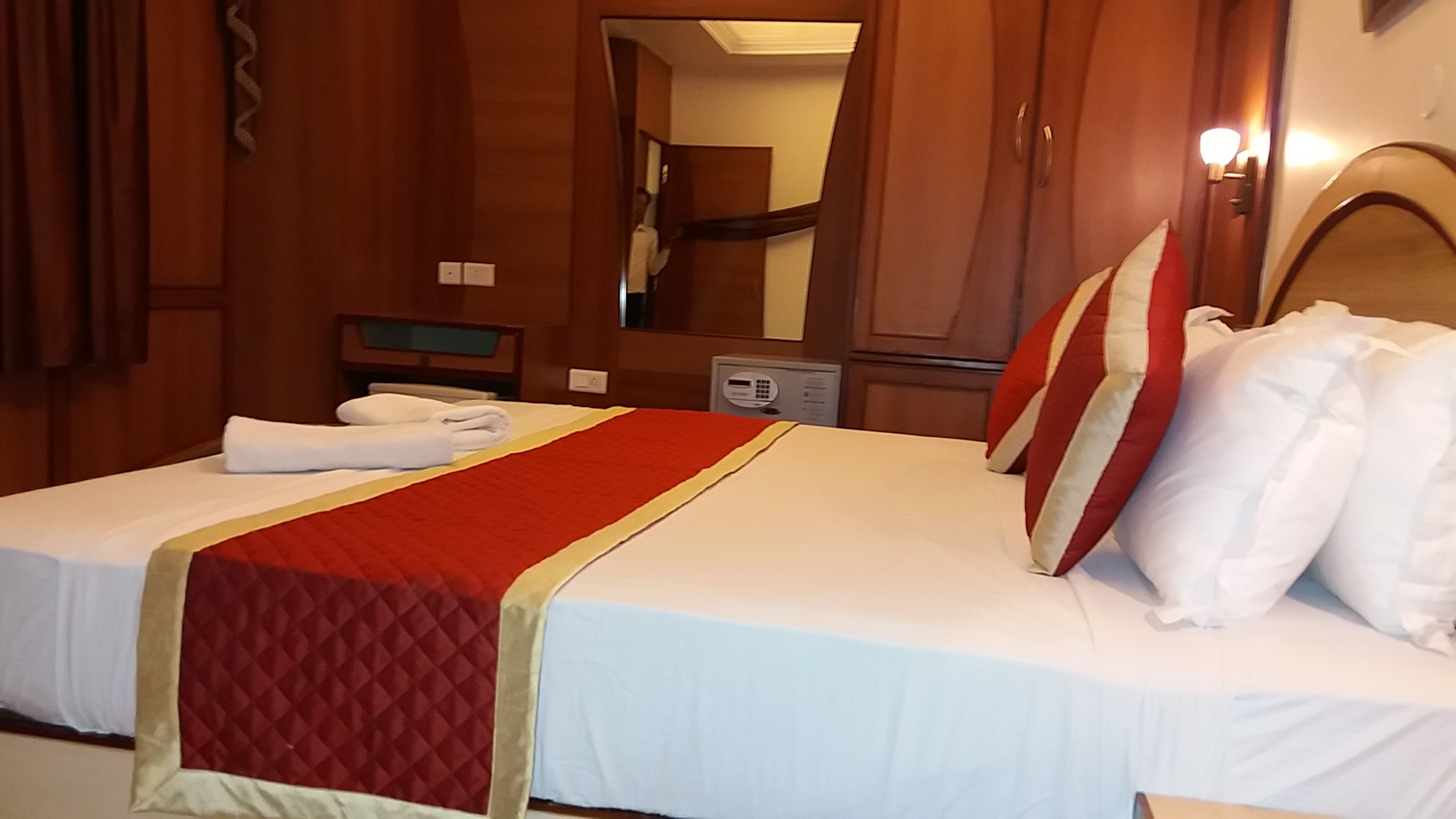 A hotel room with a bed, a mirror, a bedside table, and a telephone.