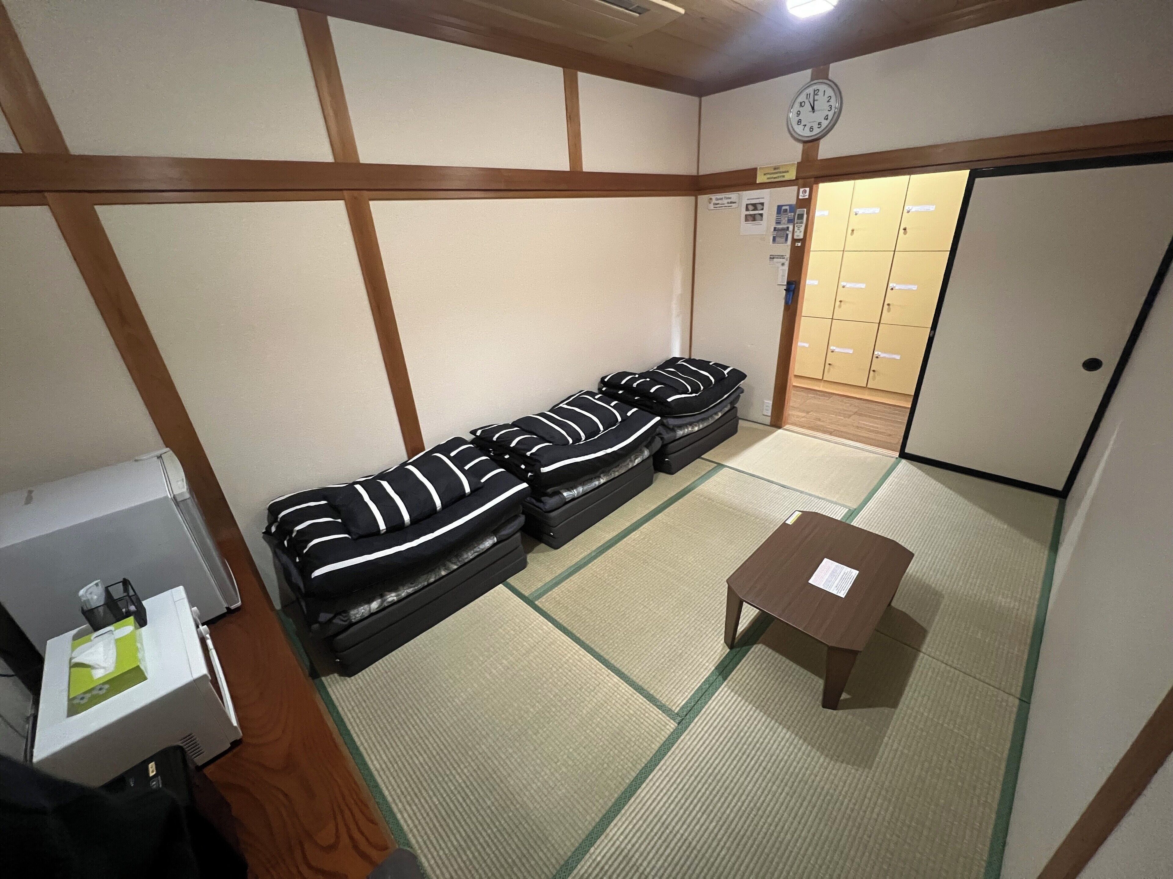 Quarto com piso de tatame, um sofá listrado em preto e branco, uma pequena mesa de madeira e um relógio na parede.