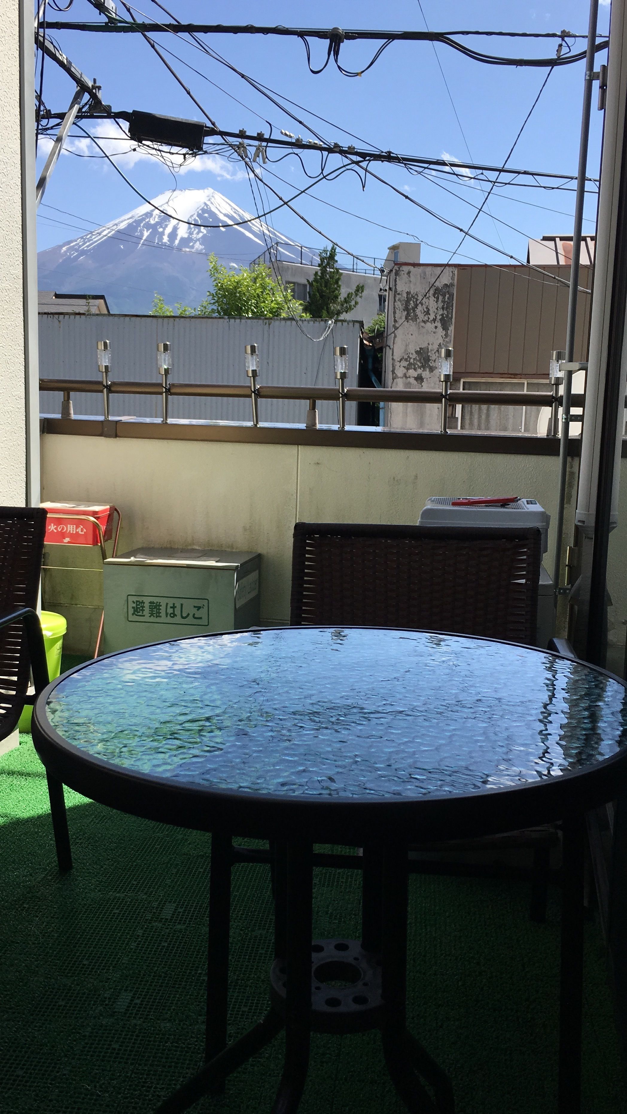 A round glass table with chairs, a green mat, and a view of a mountain.