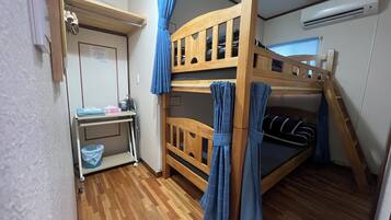 A bunk bed room with a desk and chair, a small trash bin, and a window with curtains.