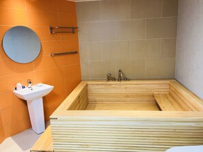 Un baño moderno con una bañera de madera, un lavamanos blanco y un espejo redondo.