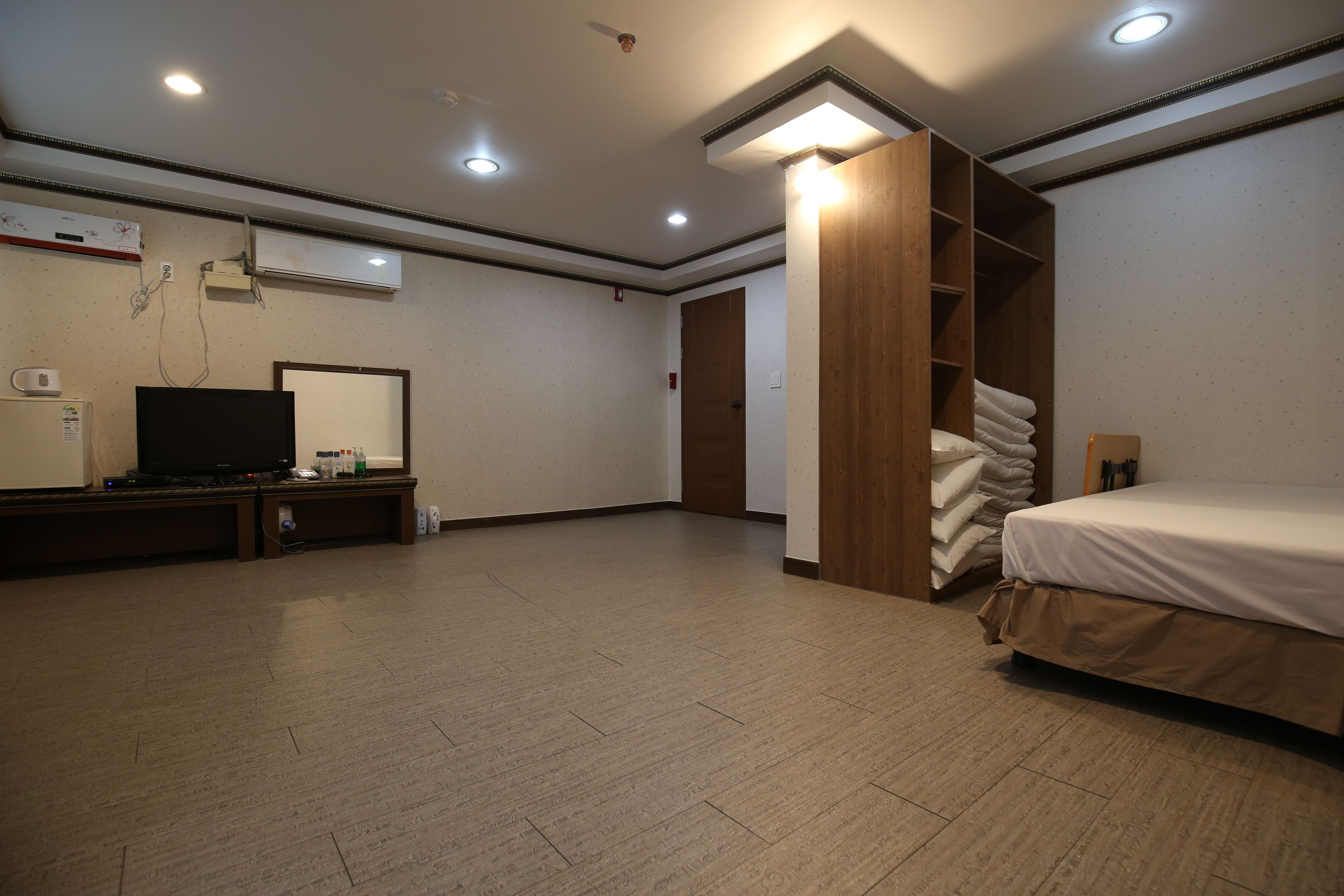 A hotel room with a bed, a TV, a wardrobe, and a desk with a computer.