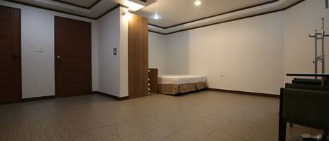 A spacious room with a wooden floor, a bed, a chair, and a wardrobe.