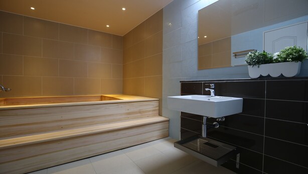 A modern bathroom with a wooden bathtub, a white sink, and a black tiled wall. - R.I Spa Hotel (Chungju)