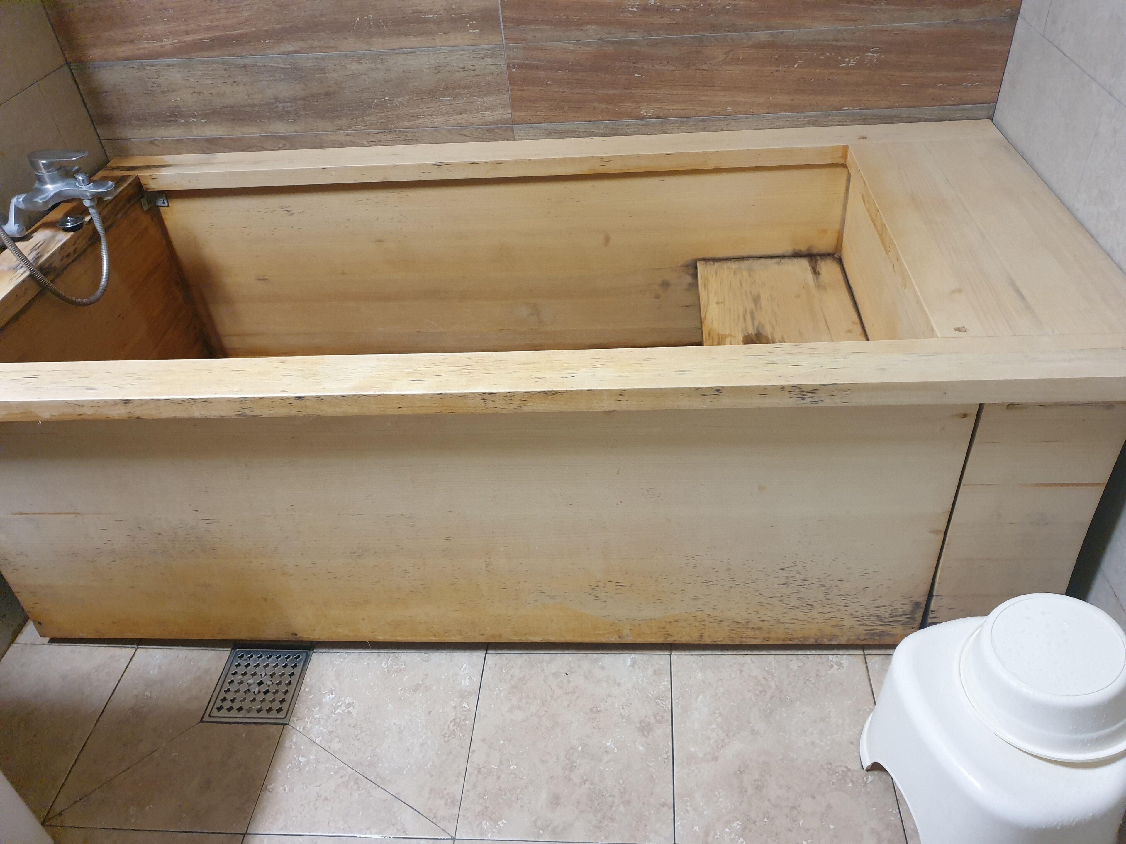Eine hölzerne Badewanne in einem Badezimmer mit gefliestem Boden und einer weißen Toilette.