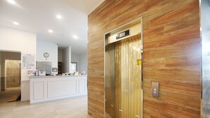 A reception area with a wooden wall, a reception desk, and an elevator. - R.I Spa Hotel (Chungju)