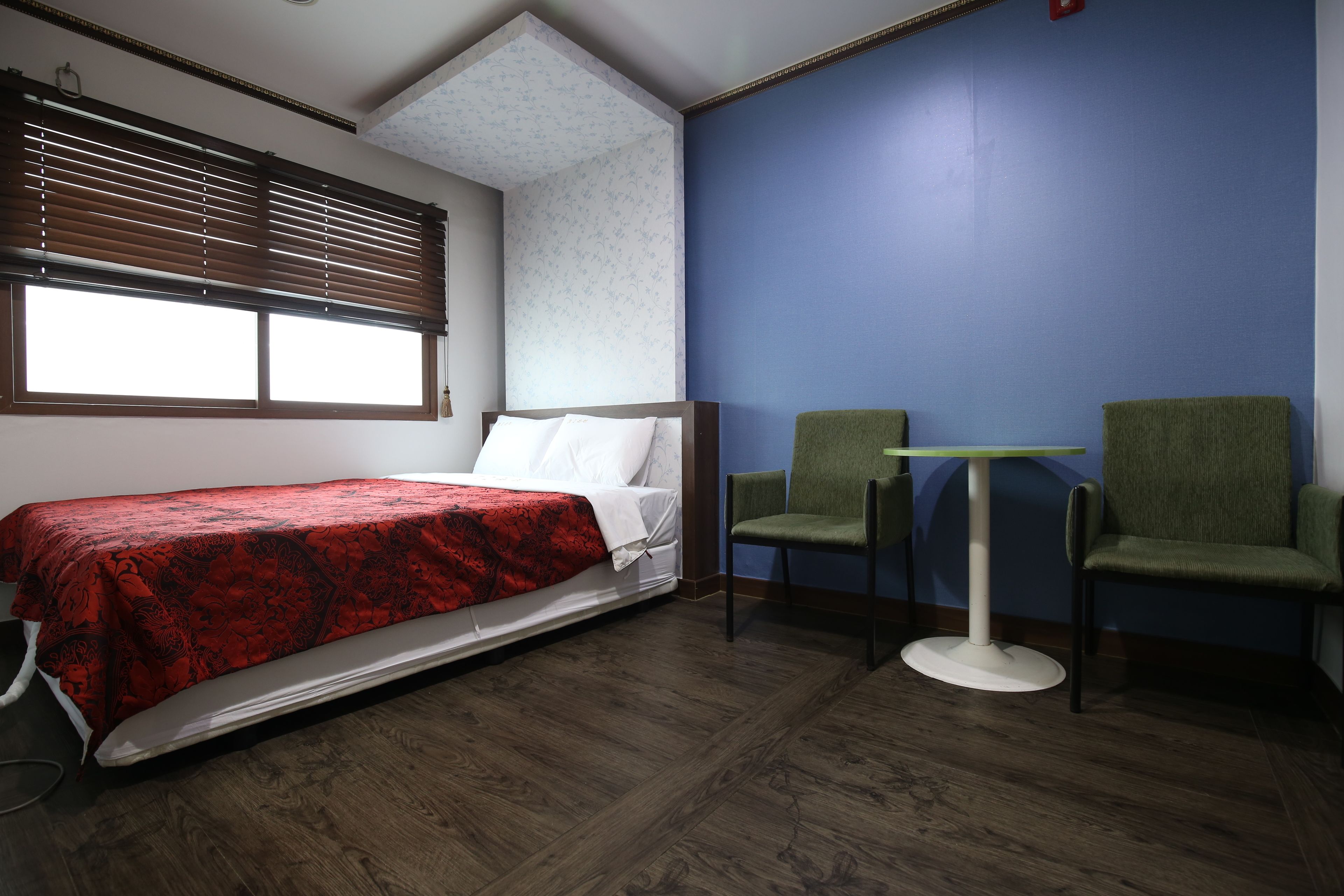 Una habitación con cama, dos sillas, una mesita y una ventana con persianas.