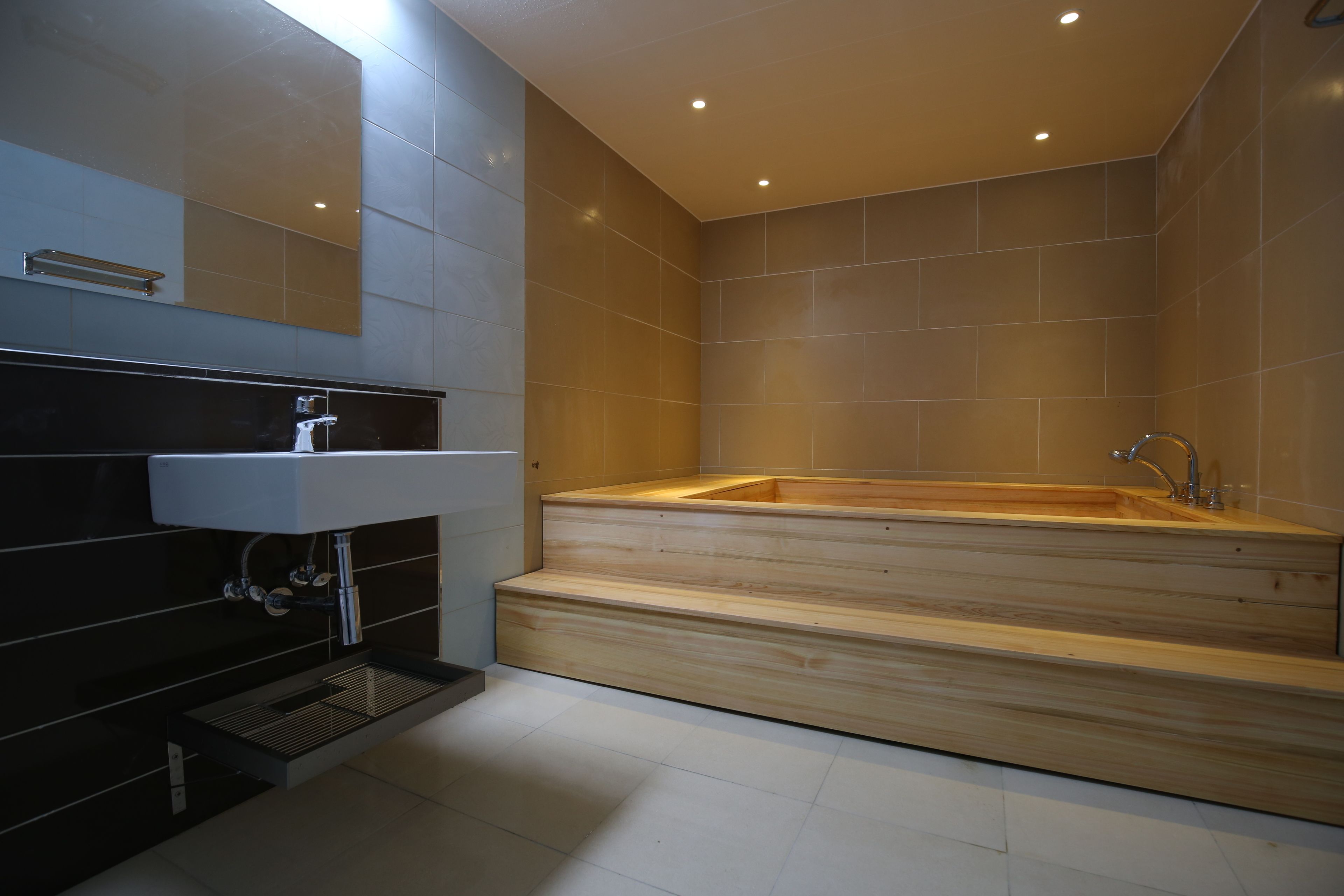 A modern bathroom with a wooden bathtub, a white sink, and a mirror above the sink.