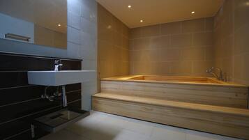 A modern bathroom with a wooden bathtub, a white sink, and a mirror above the sink.