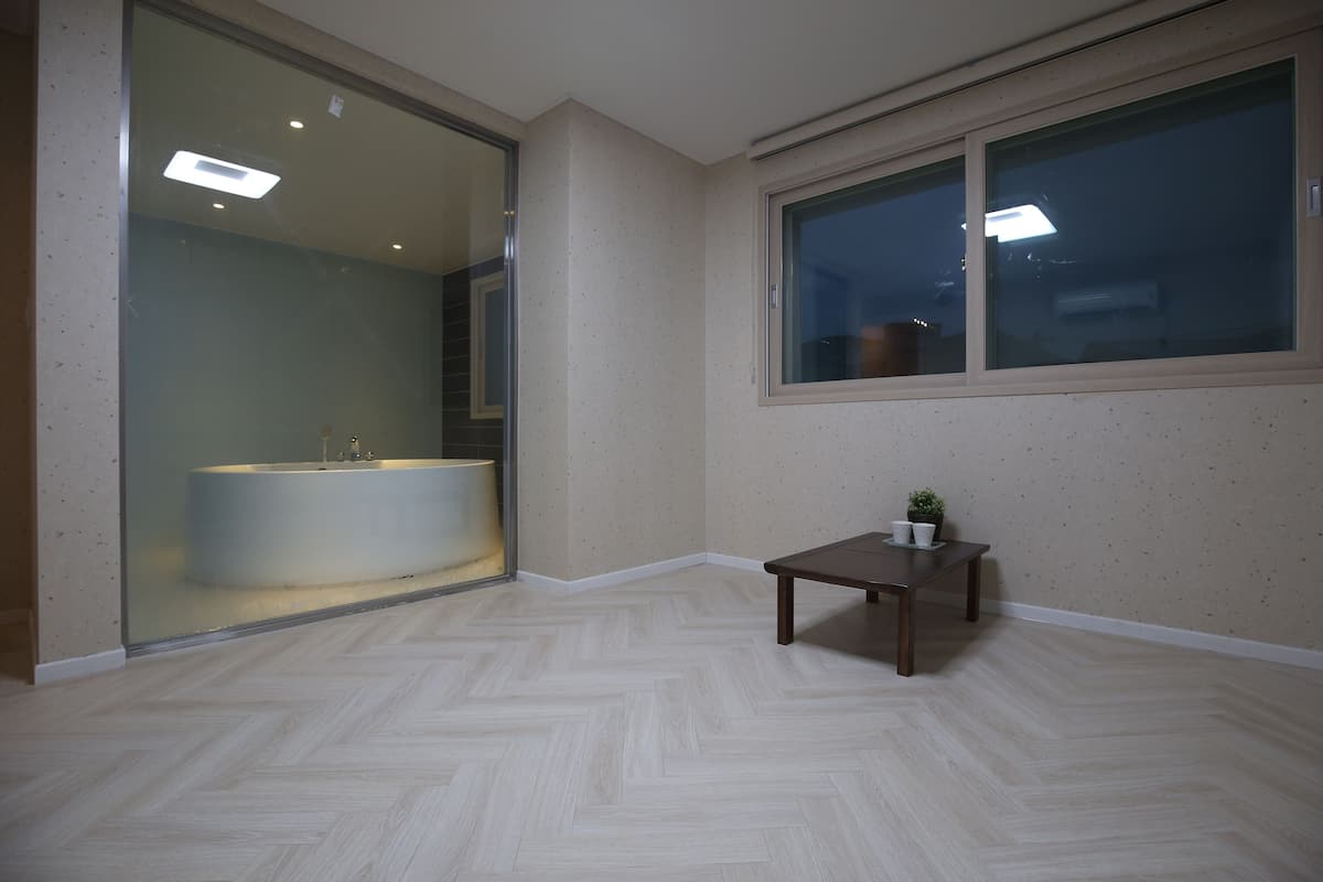 A room with a herringbone floor, a glass shower enclosure, a small wooden table, and a window with a view.