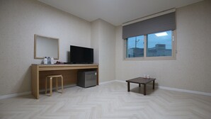 A room with a wooden desk, a television, a small table, and a window with a view of buildings. - R.I Spa Hotel (Chungju)