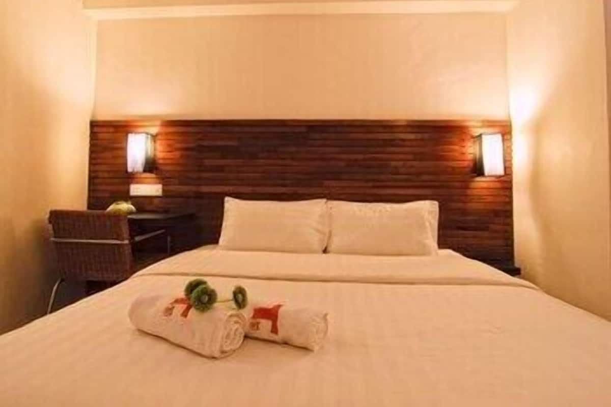 A hotel room with a bed, two bedside lamps, a wooden headboard, and a small table with a chair.