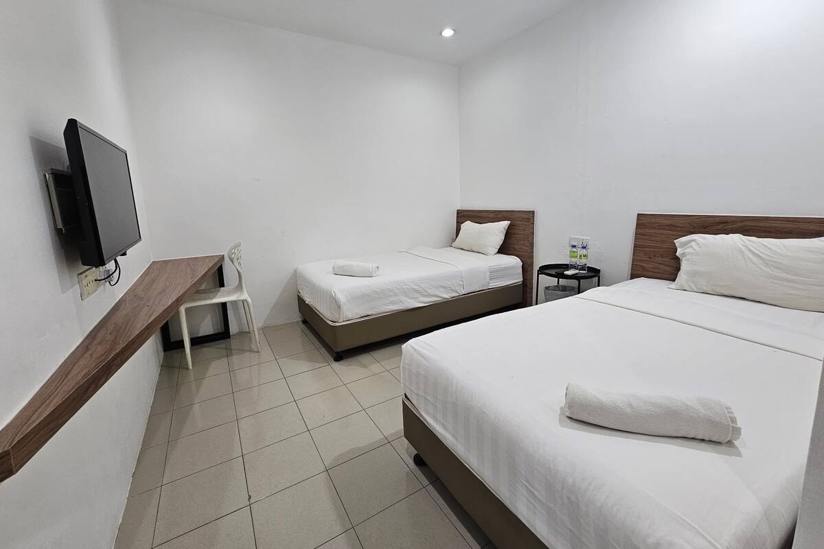 A hotel room with two beds, a TV, a chair, and a small table with a bottle.