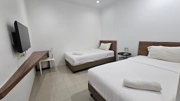 A hotel room with two beds, a TV, a chair, and a small table with a bottle.