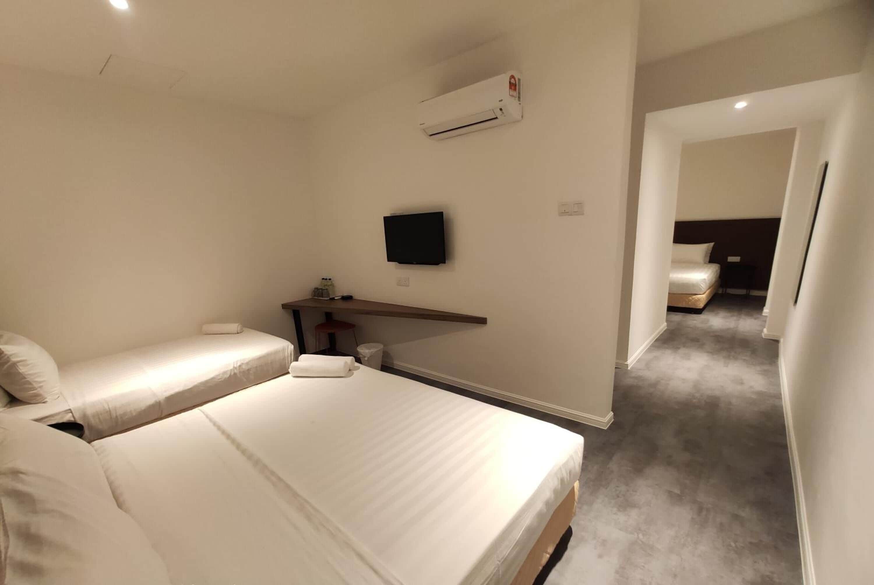 A hotel room with two beds, a TV, a desk, and an air conditioning unit.