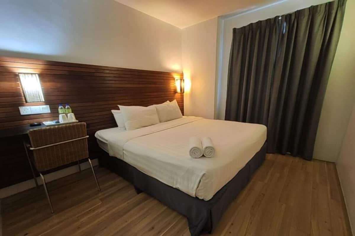 A hotel room with a wooden headboard, a bed with white linens, a bedside table with a lamp, and a window with curtains.