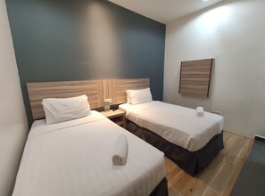 A hotel room with two beds, each with white linens and a rolled towel. There is a wooden headboard on the left bed, and a wall-mounted shelf with a lamp and a small table. - T Hotel Tandop (Alor Setar)