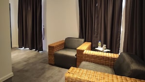 Una sala de estar moderna con un sofá gris, dos sillones de mimbre y una mesita auxiliar con una botella y un vaso.