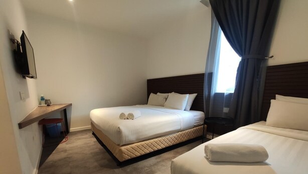 Habitación de hotel con dos camas, televisión montada en la pared, un escritorio pequeño y una ventana con cortinas.
