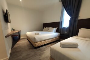 Une chambre d’hôtel avec deux lits, un téléviseur fixé au mur, un petit bureau et une fenêtre avec des rideaux.