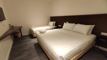A hotel room with two beds, a wooden headboard, a small table with a bottle, and a trash bin.