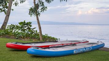 Two kayaks on a grassy area near a body of water with trees in the background.