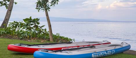 Two kayaks on a grassy area near a body of water with trees in the background.