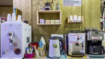 A coffee station with various brewing machines and a shelf with cups and a sign.