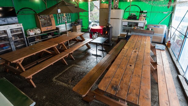 Un espacio de comedor al aire libre de estilo rústico, con bancos y mesas de madera, una estufa pequeña y un refrigerador.