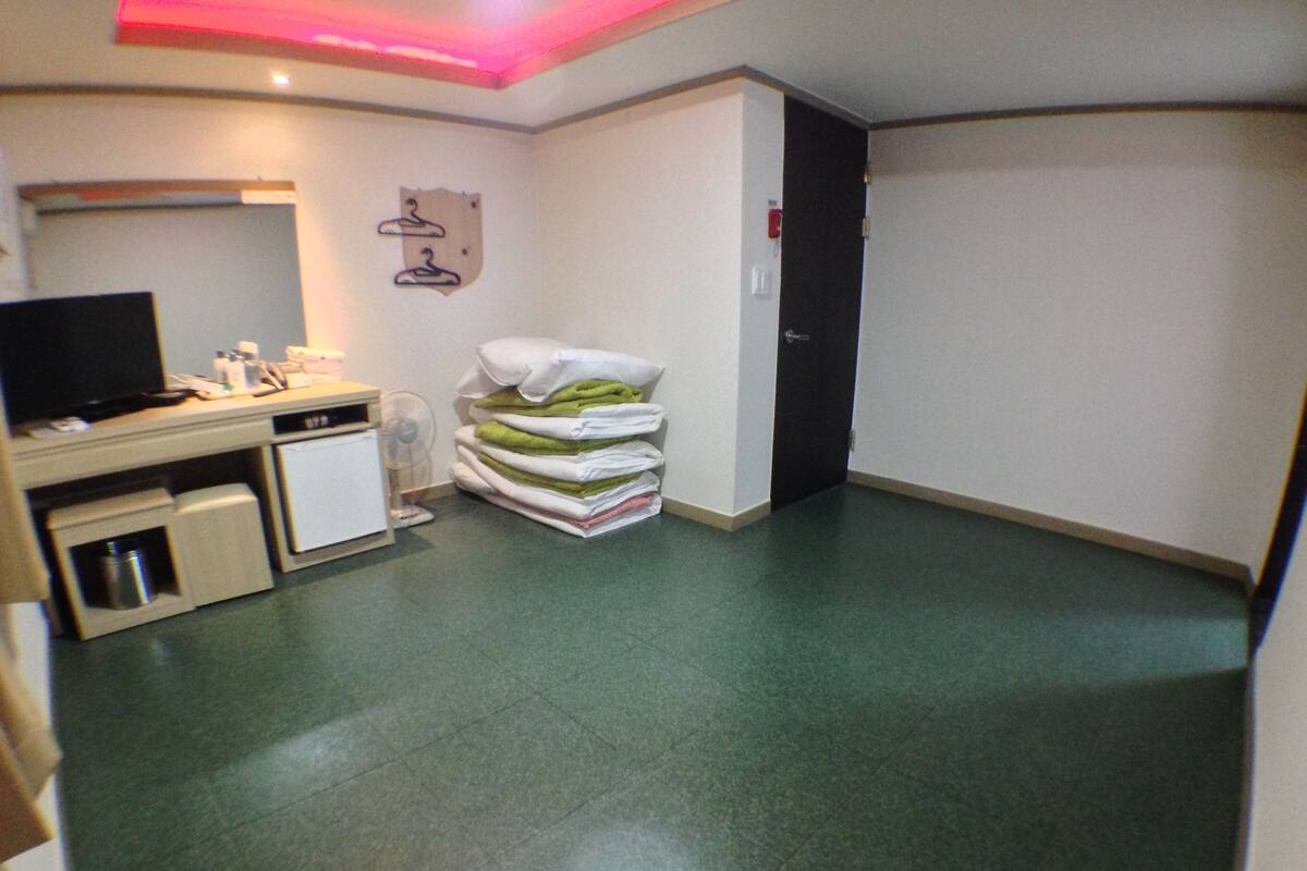 A hotel room with a kitchenette, a bed, a TV, and a fan.